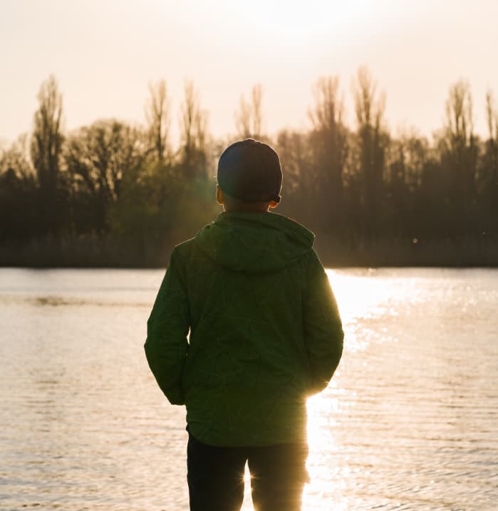 A young man standing alone at the water's edge